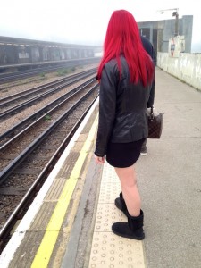 A woman in black standing on a train platform.